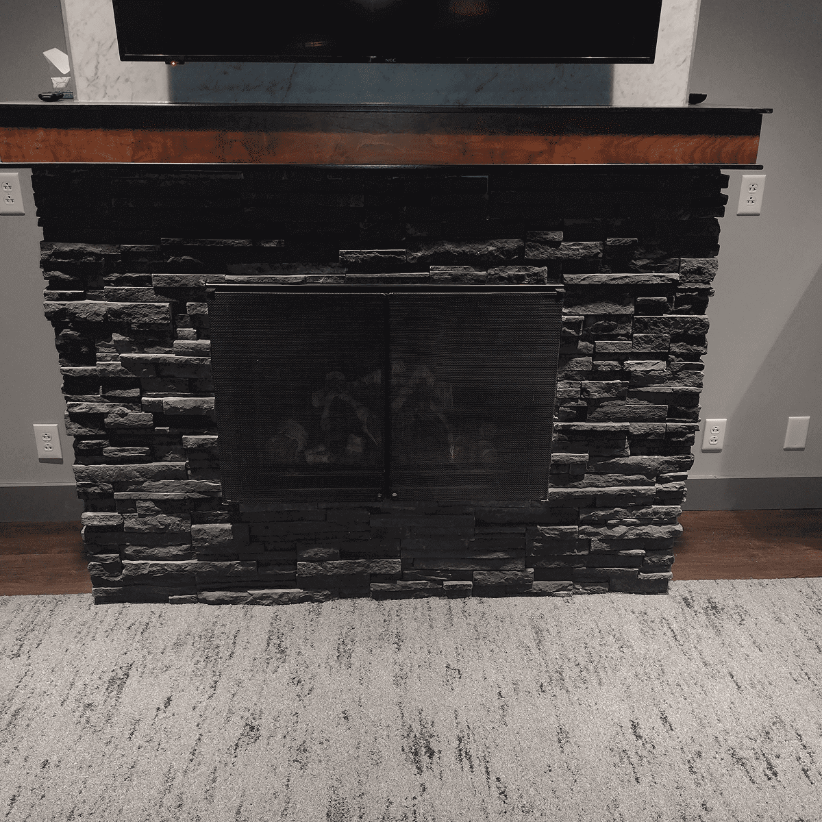 Modern stone fireplace with a wooden mantel and carpeted floor.